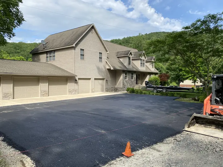 Fresh asphalt parking pad at a large home with wooded Ozark hills behind it