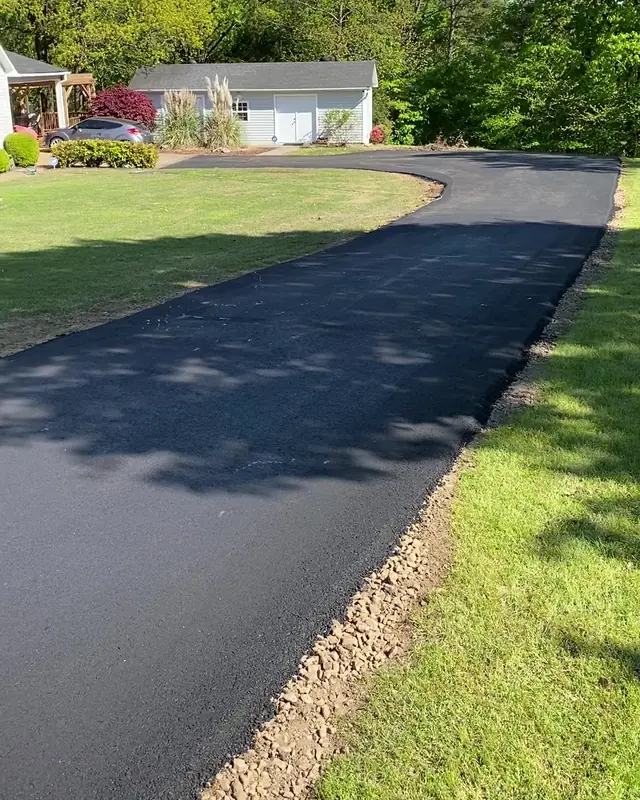New black asphalt driveway curving past a lawn, shortleaf pines, and a white garage in the Arkansas River Valley