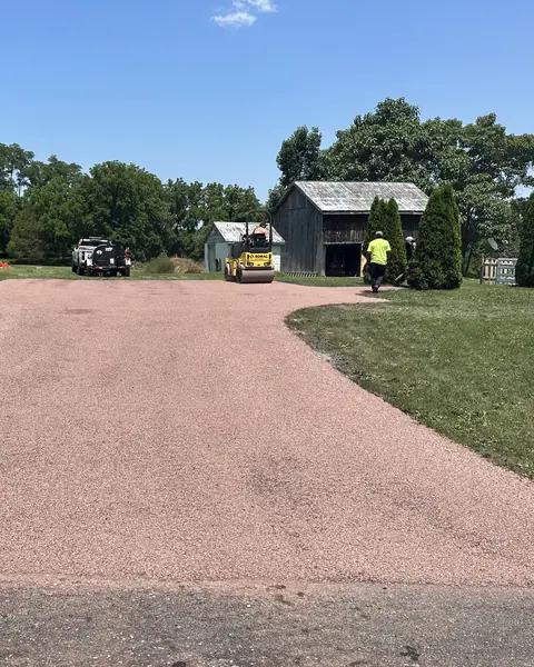 Roller and crew finishing a red stone chip seal driveway