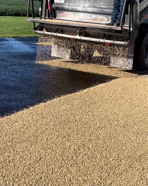 Dump truck spreading crushed stone chips over fresh black binder